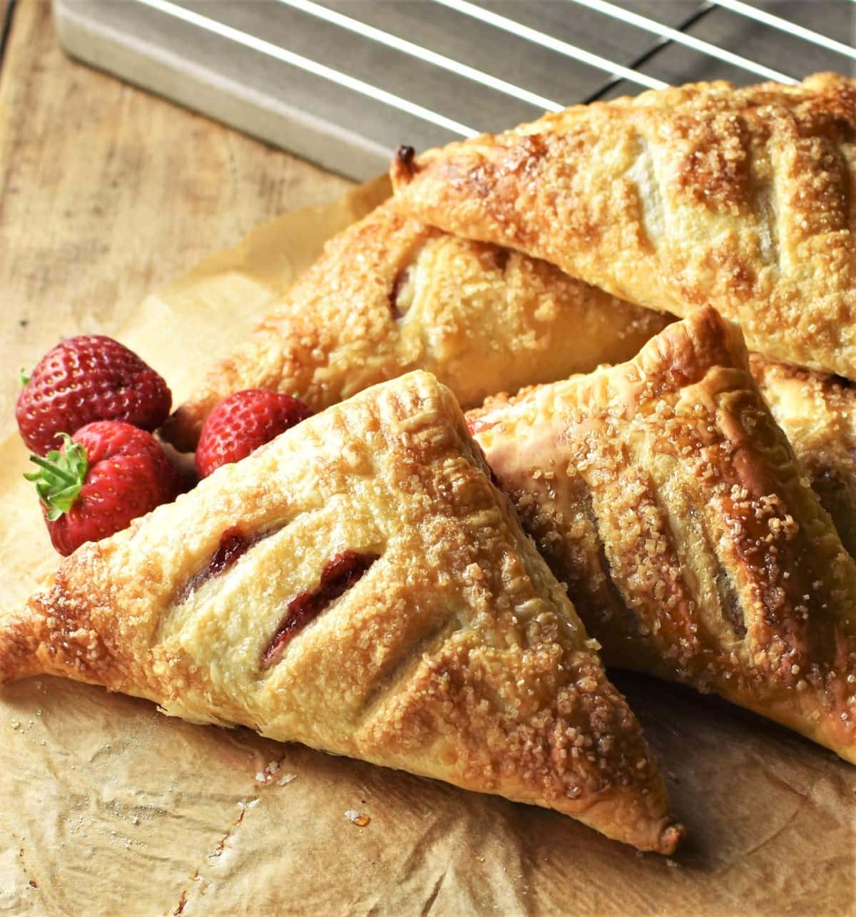 Side view of strawberry turnovers on top of parchment with fresh strawberries in background.