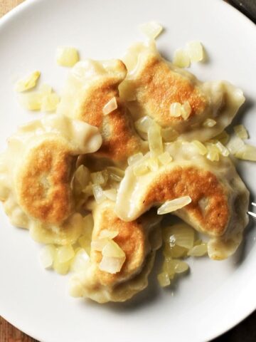 Fried vegan pierogi with onions on top of white plate with fork.