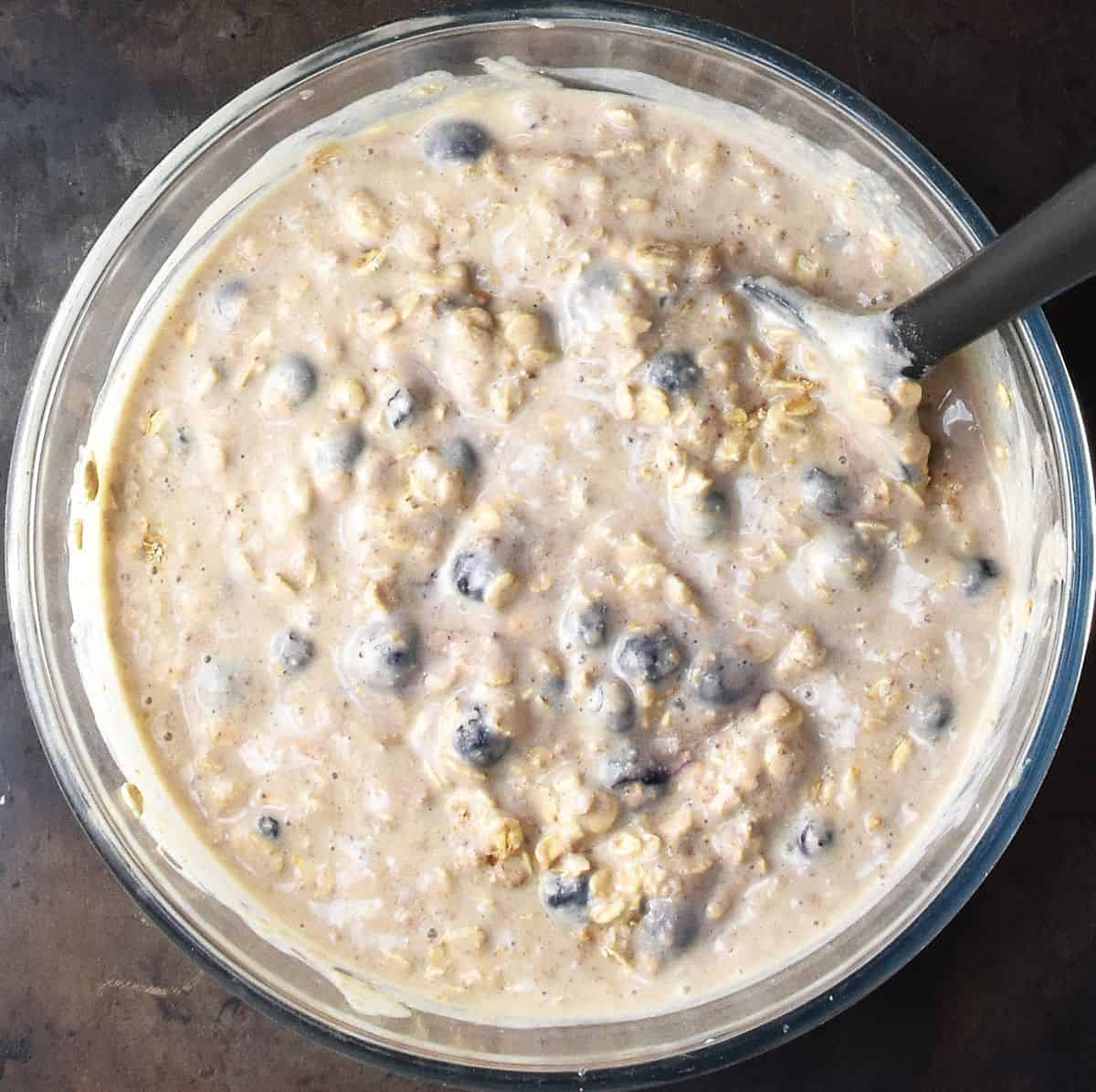 Top down view of creamy oat fruit batter in glass bowl with black spoon.