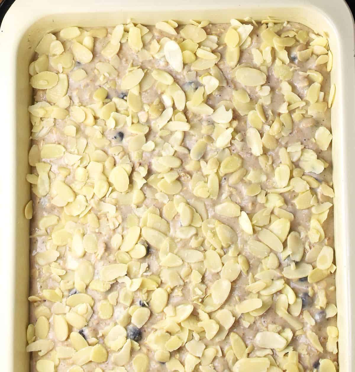 Top down view of uncooked oatmeal bake with flaked almonds on top in white pan.
