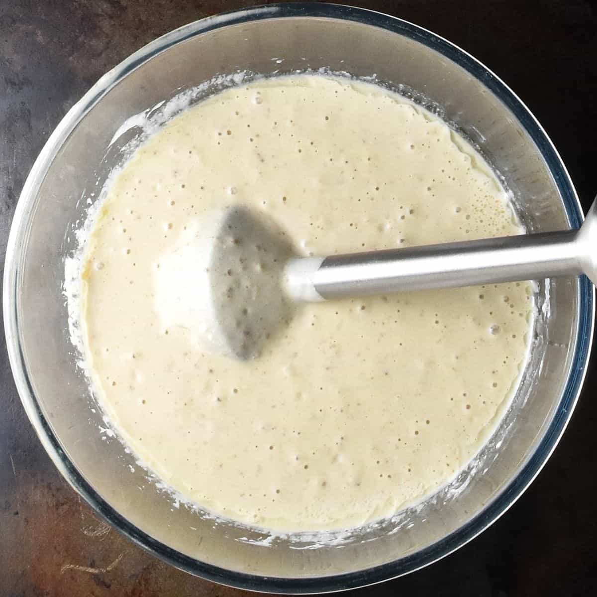 Creamy mixture with stick blender in large, glass bowl.