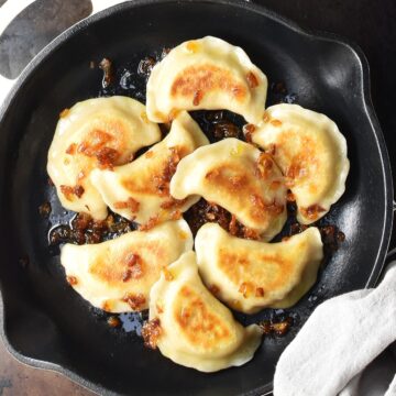 Top down view of browned vegan pierogi with onion incast iron skillet.