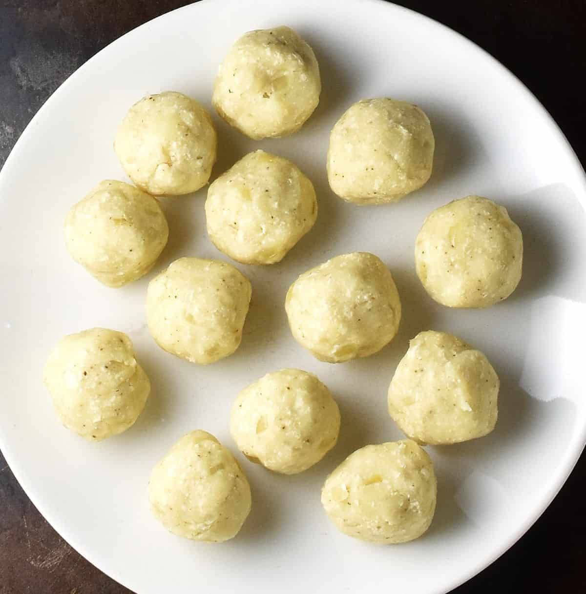 Top down view of vegan pierogi filling balls on white plate.