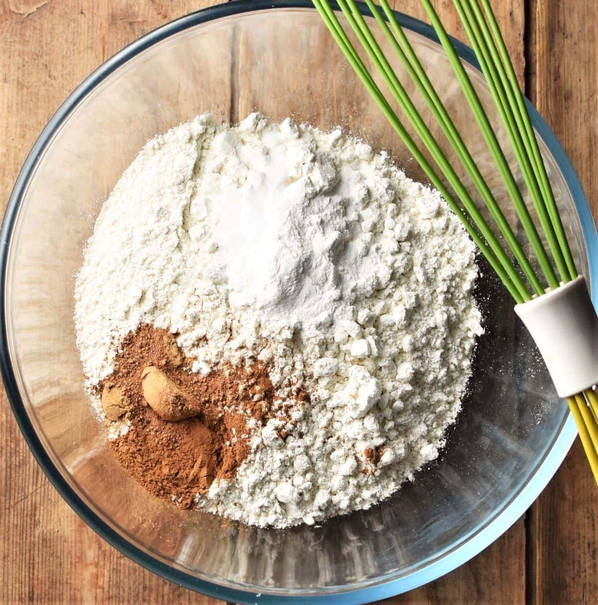 Carrot cake dry ingredients in mixing bowl with green whisk.