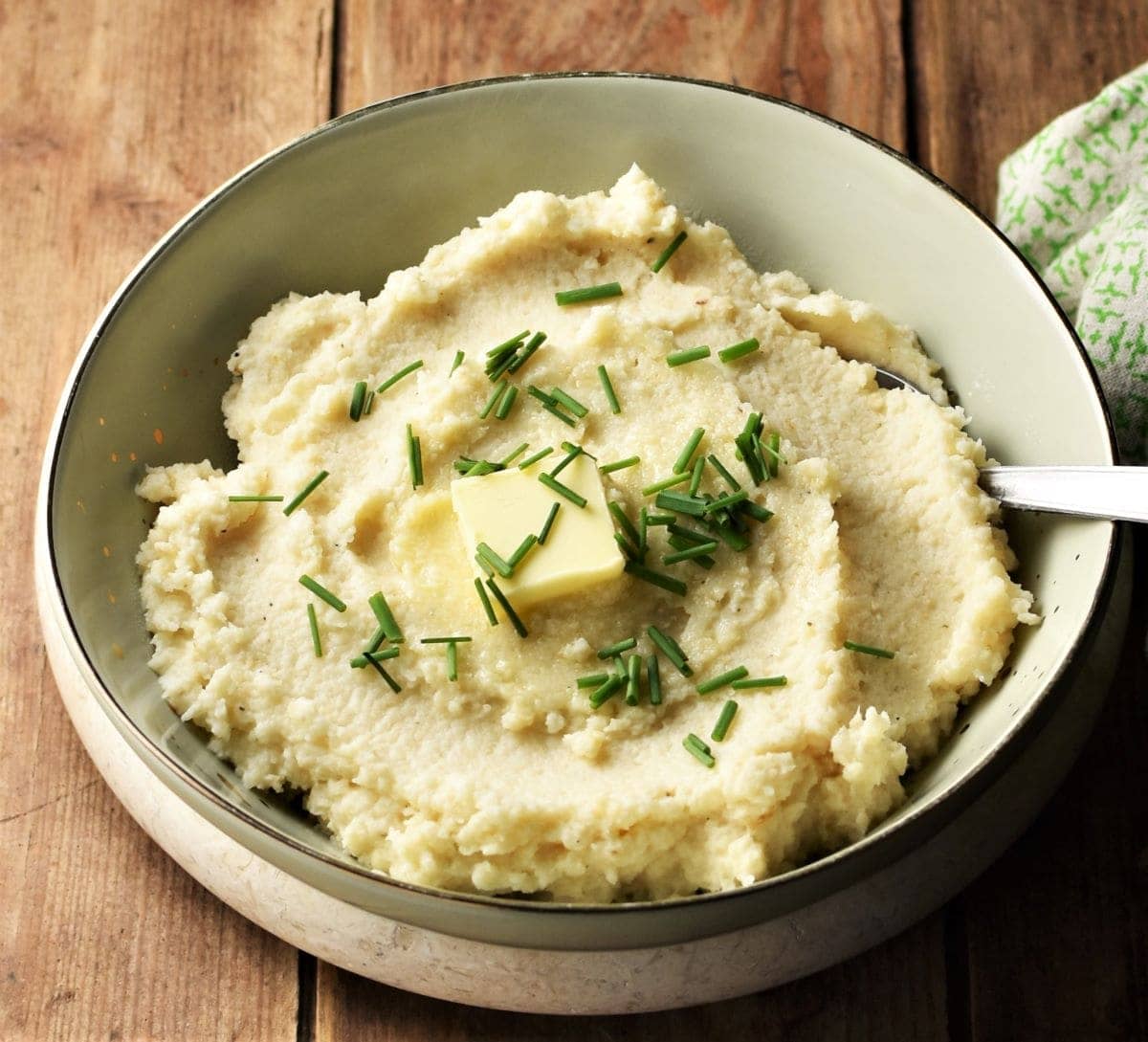 Side view of celery root puree with butter and chives in green bowl.