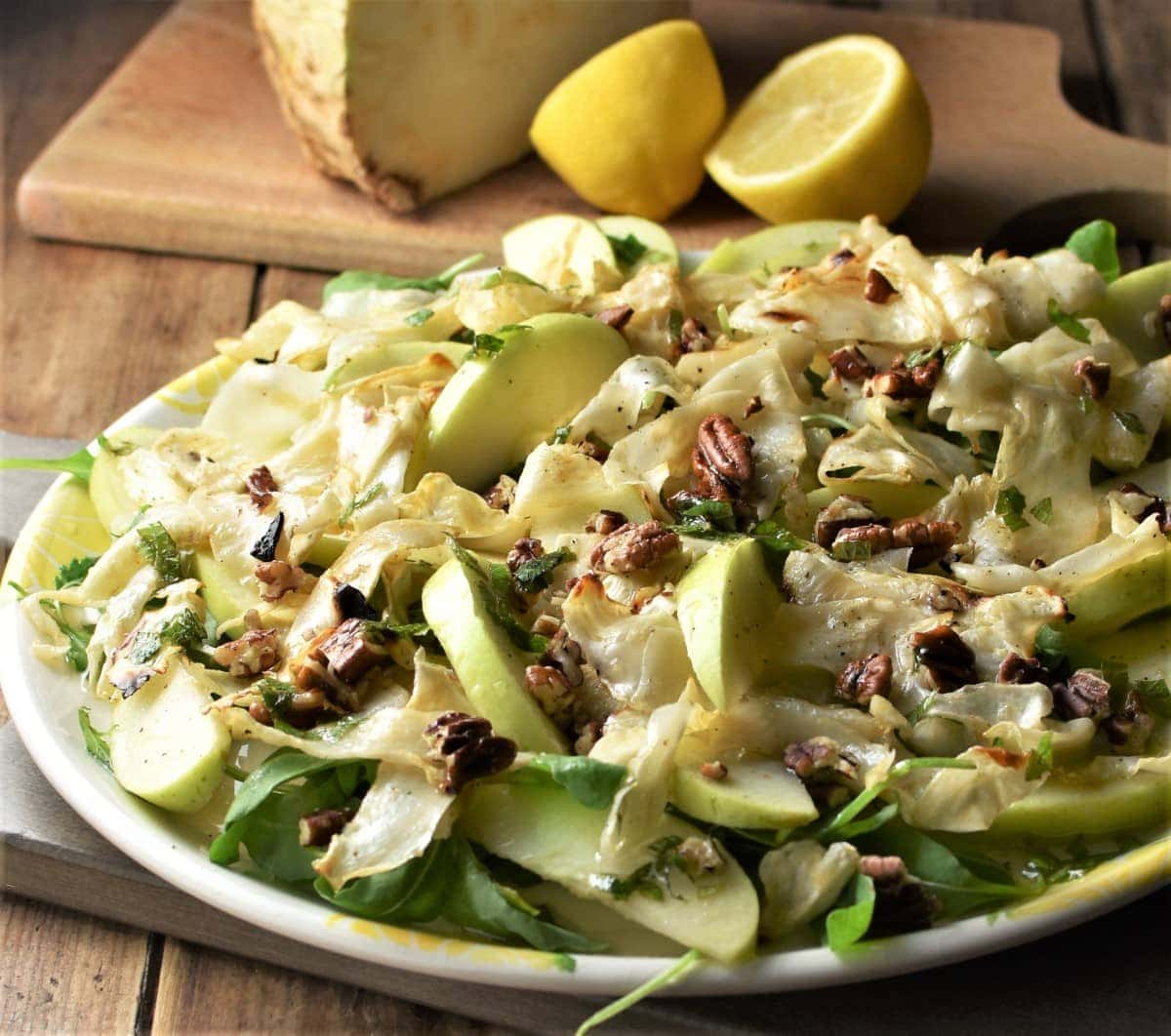 Side view of celeriac apple salad on large plate with lemon in background.