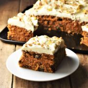 Side view of low fat carrot cake slice on white plate with cake in background.