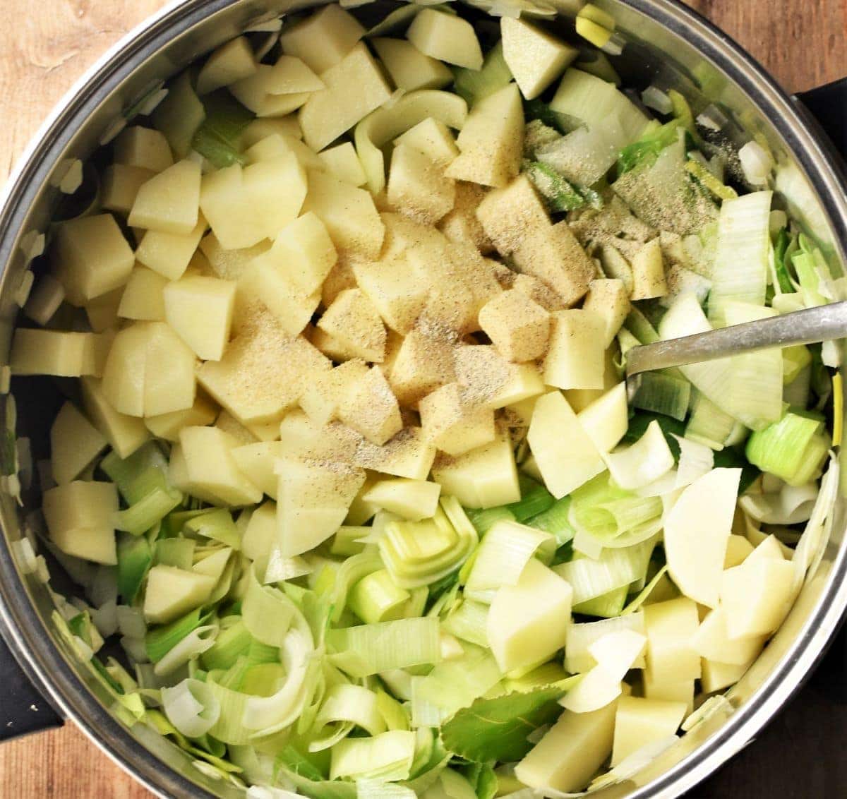 Diced potatoes and chopped leeks in large pot with spoon.