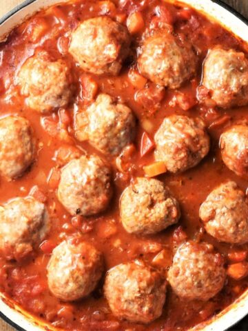 Top down view of meatballs in chunky vegetable sauce in white round dish.