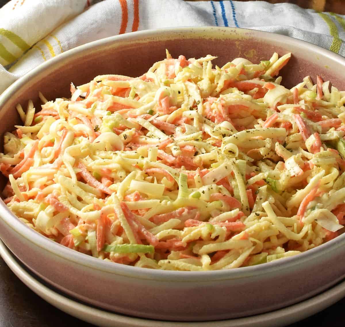 Side view of creamy celeriac salad in pink bowl with cloth in background.