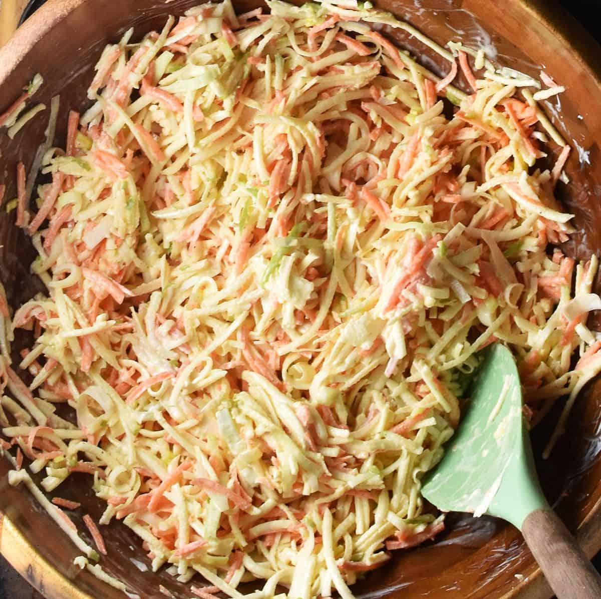Tossing Polish celeriac salad in wooden bowl with green spatula.