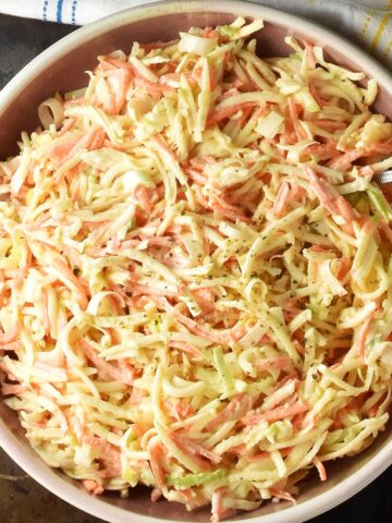 Top down view of celery root salad in rustic pink bowl with spoon.