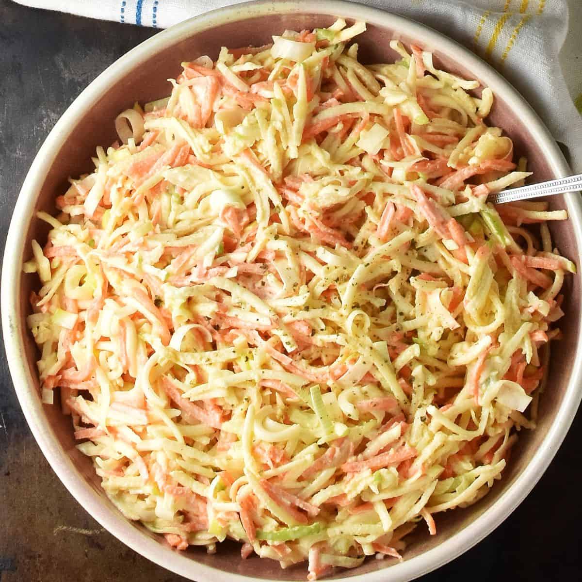 Top down view of celery root salad in rustic pink bowl with spoon.