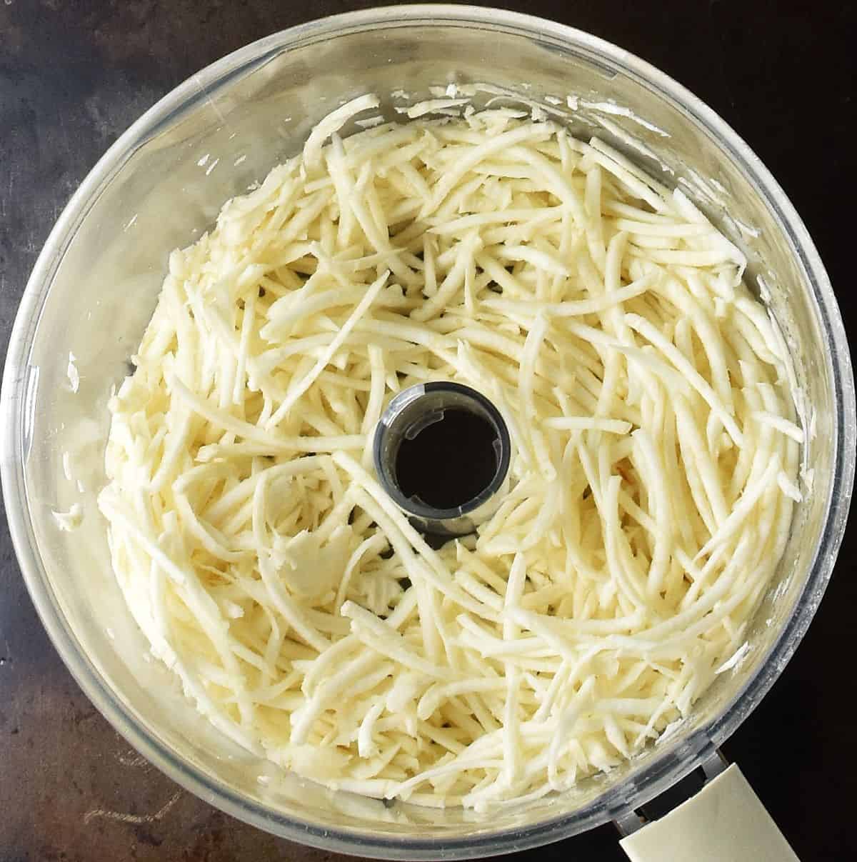 Shredded celery root in food processor bowl.