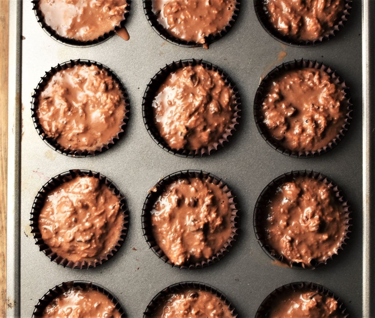 Chocolate batter in paper cases in muffin pan.