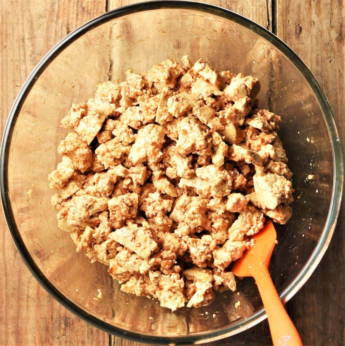 Crumbled tofu with marinade in mixing bowl with spatula.