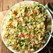 Top down view of pomelo salad with noodles, avocado and herbs on white plate.