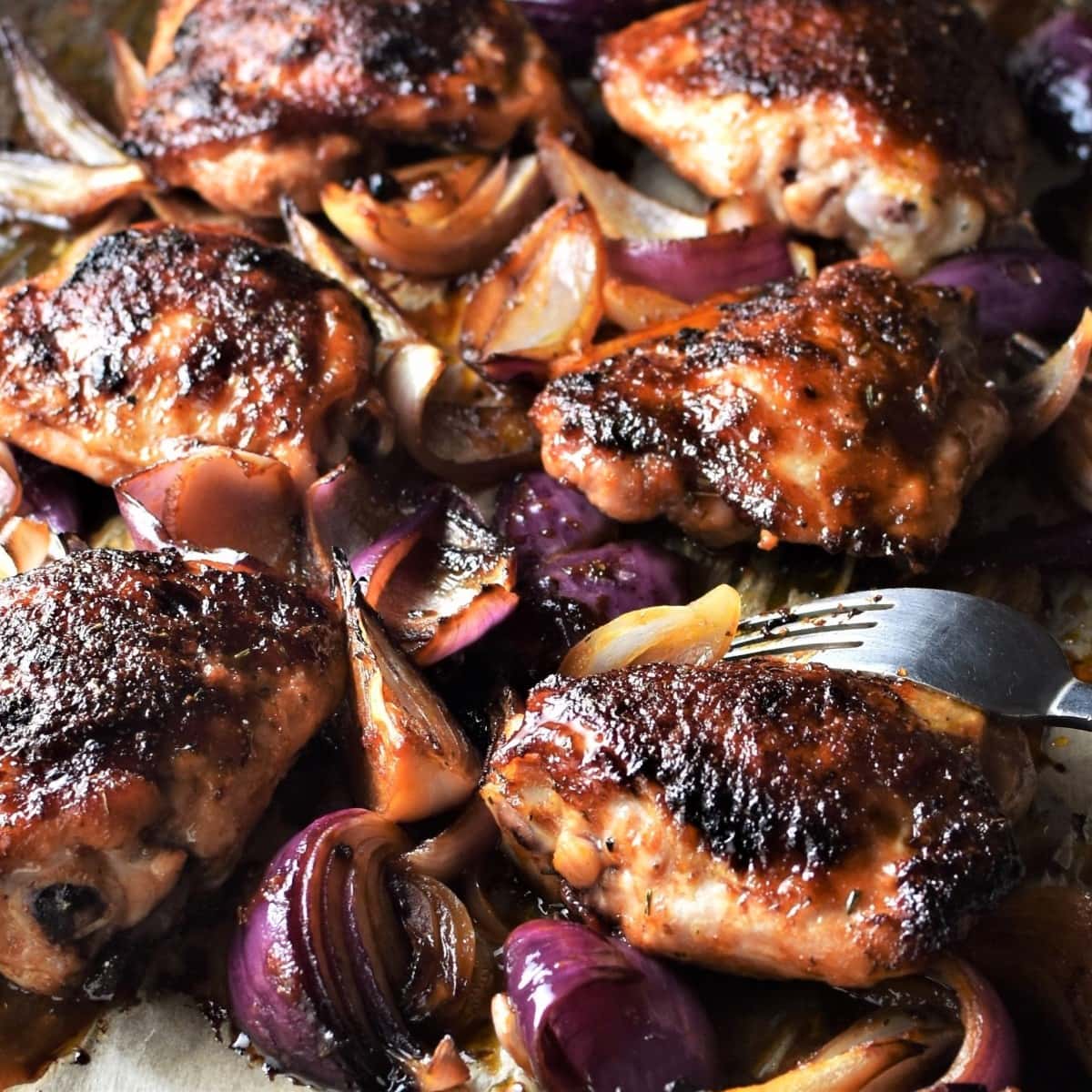 Side view of roasted sheet pan chicken thighs with onions.