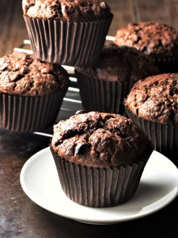 Side view of chocolate sweet potato muffins on plate and rack.