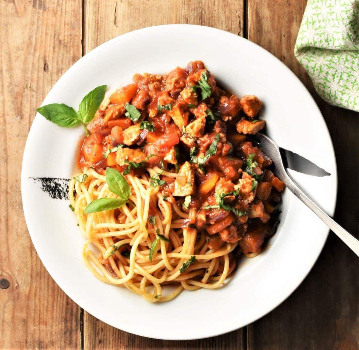 Top down view of tofu bolognese sauce with spaghetti on white plate with fork.