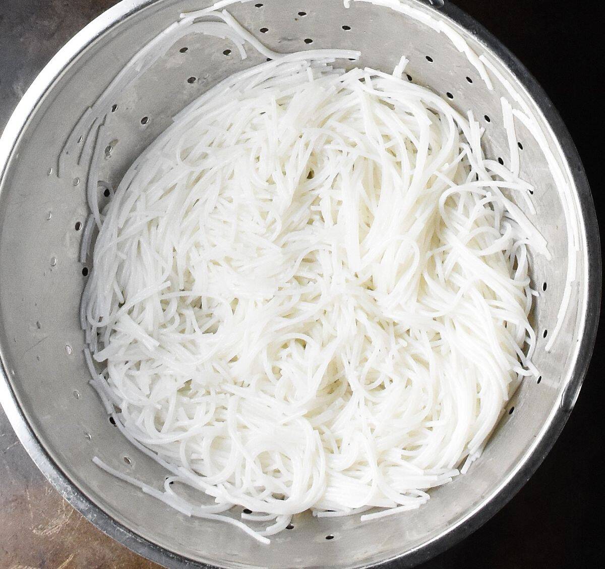Rehydrated rice noodles in metal strainer.
