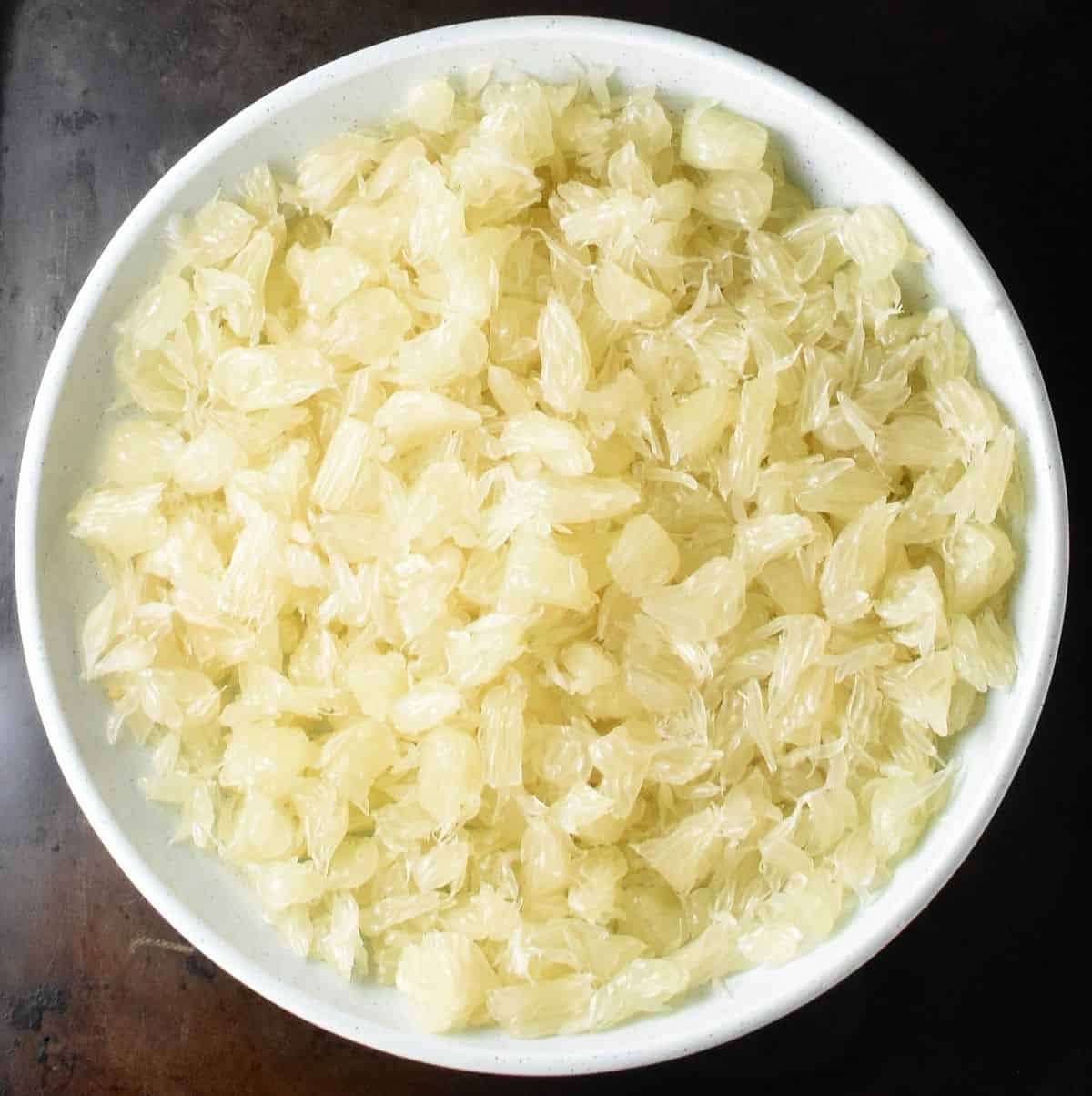 Top down view of shredded pomelo flesh in white bowl.