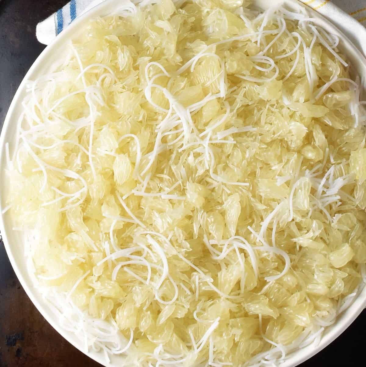 Rice noodles and crumbled pomelo flesh on white plate.