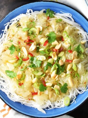 Top down view of pomelo salad with noodles, herbs and nuts in blue bowl.
