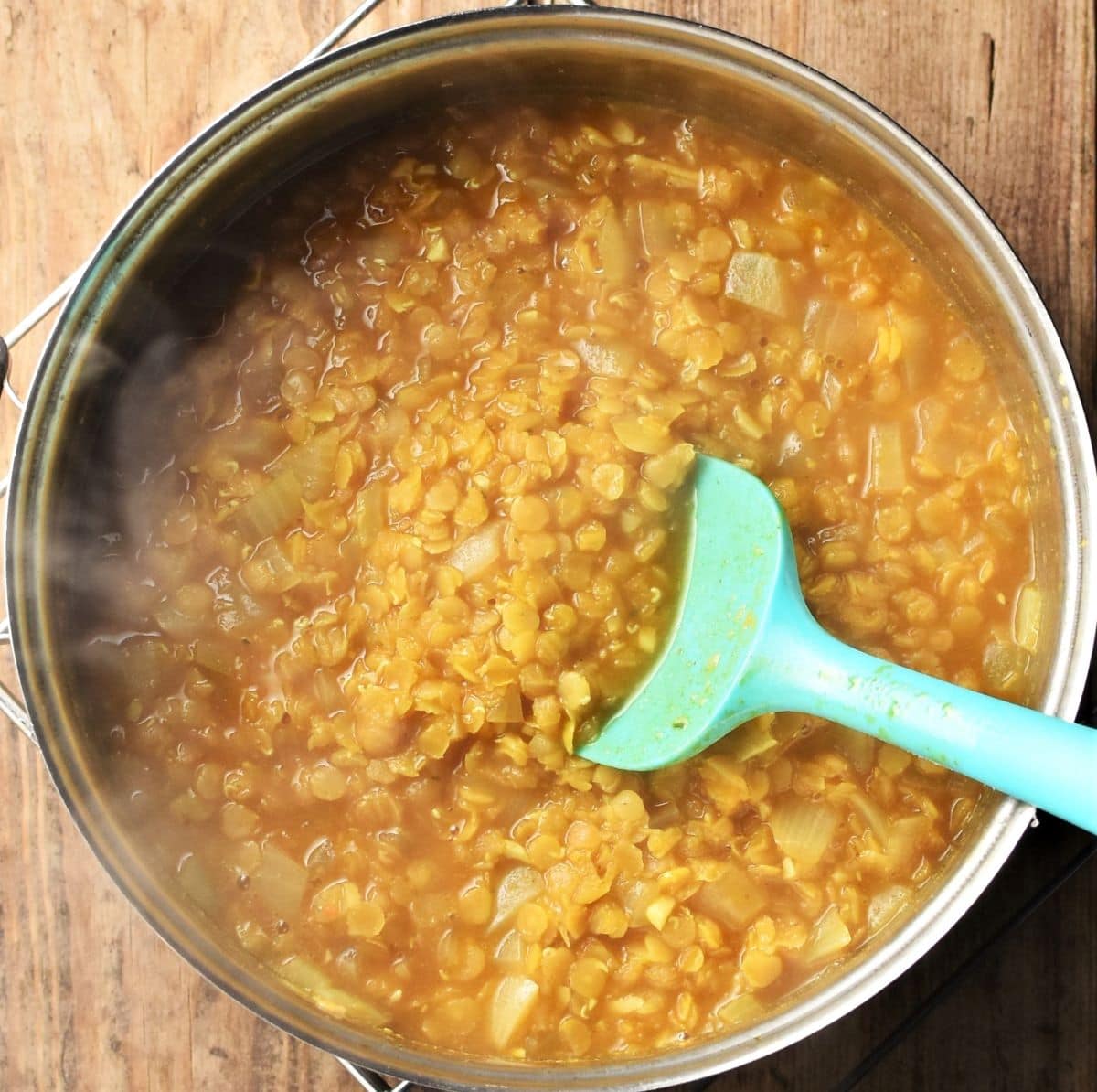 Cooking dhal in saucepan with green spoon.