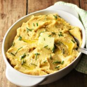 Side view of mashed rutabaga with chives in white oval dish with spoon.