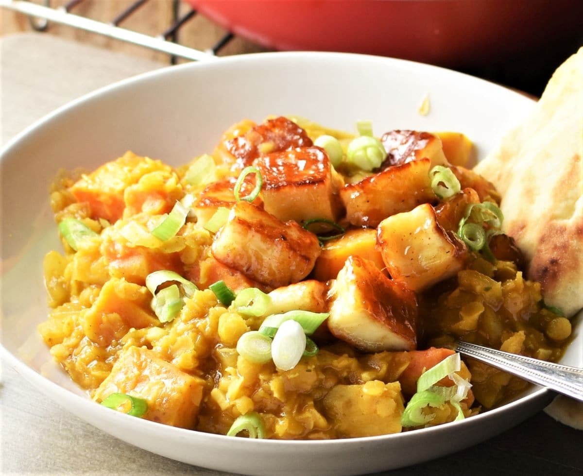Close-up side view of sweet potato dahl with halloumi in white bowl.