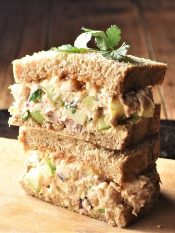 Side view of halved turkey salad sandwich stacked on top of cutting board.