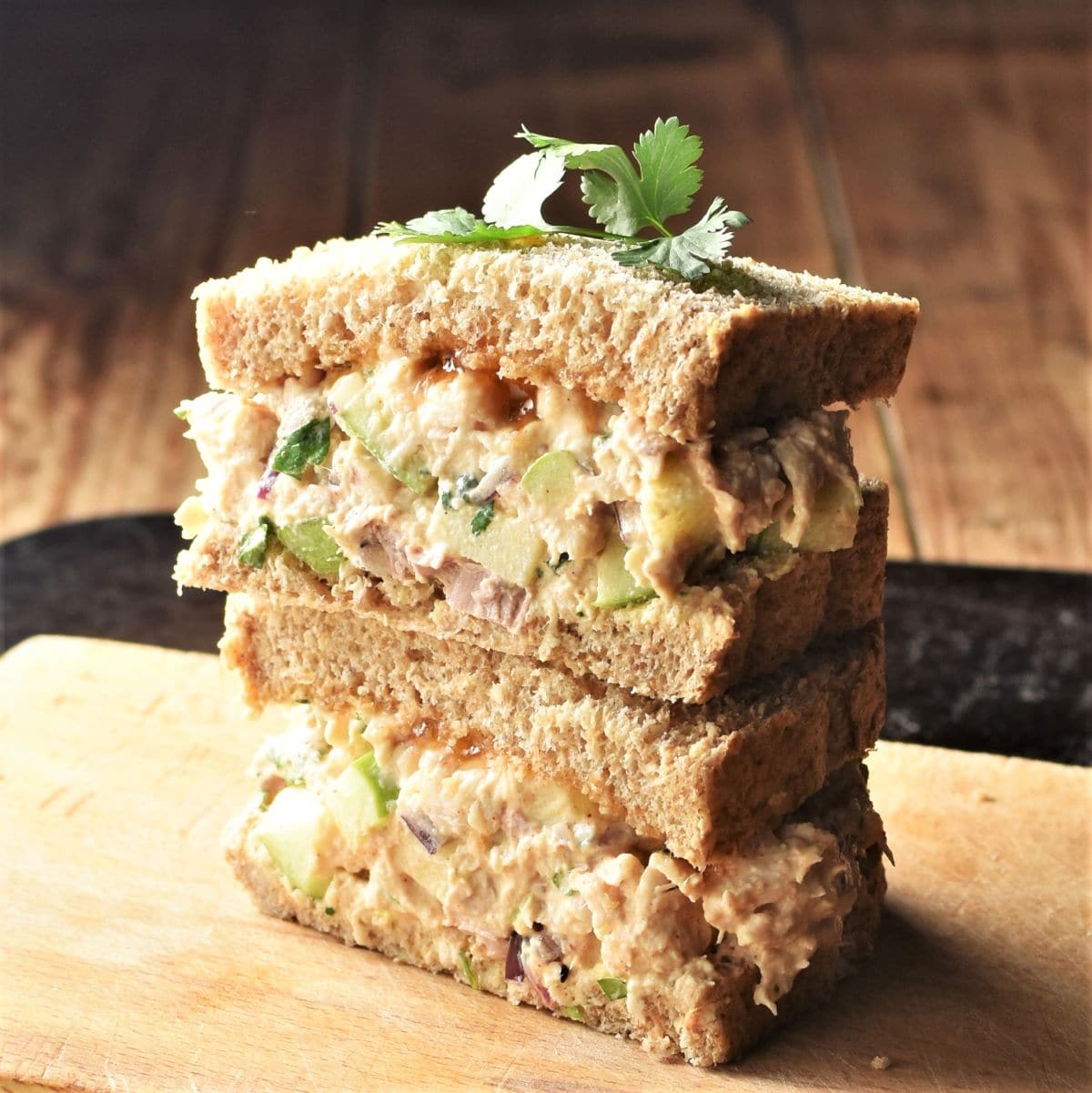 Side view of halved turkey salad sandwich stacked on top of cutting board.
