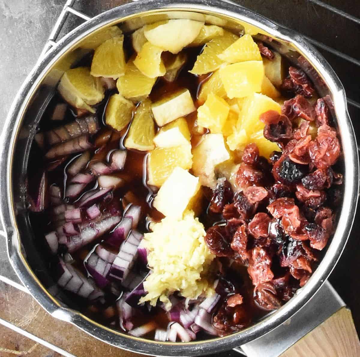 Chopped onion, orange and dried cranberries in pot.