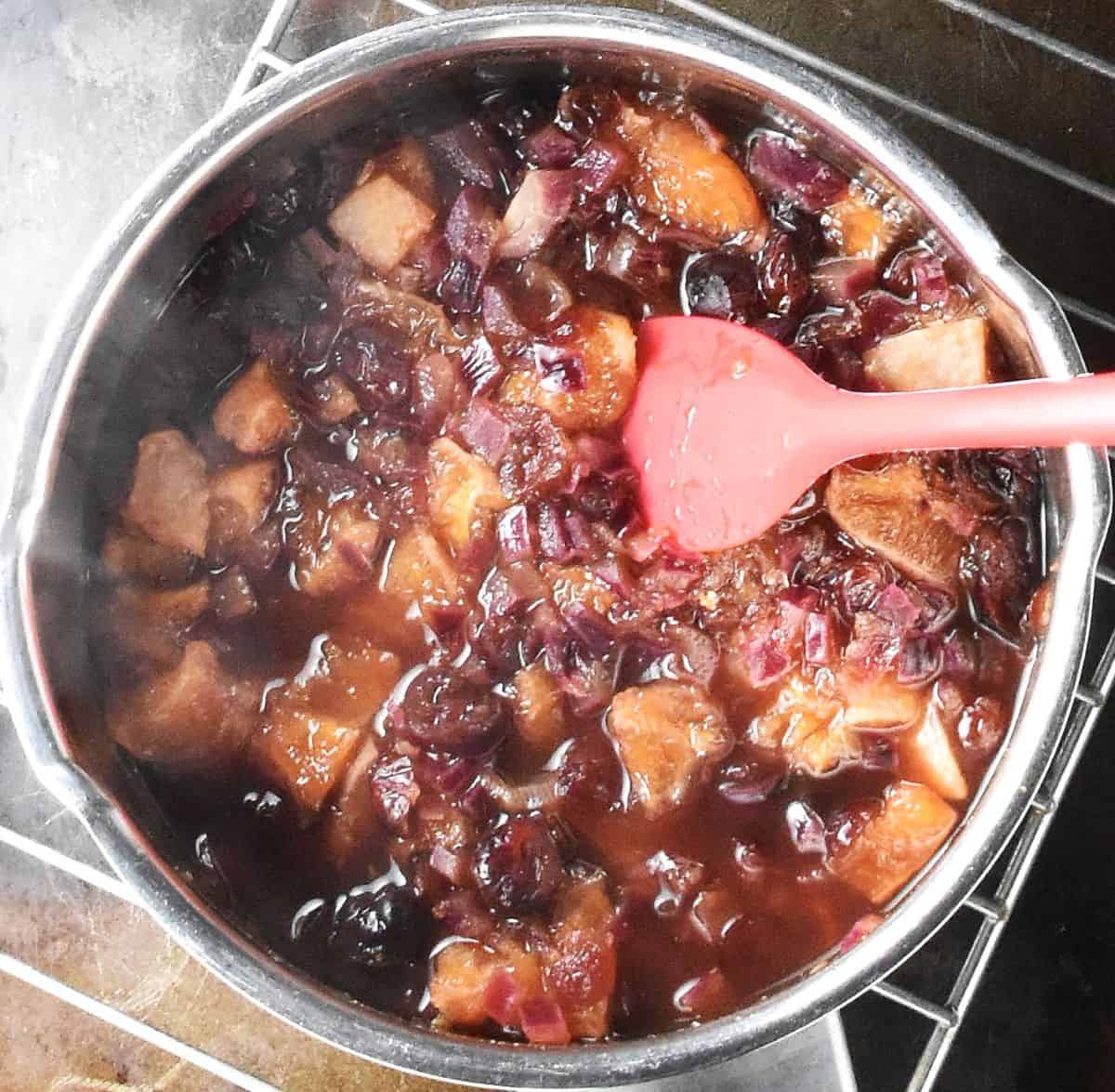 Top down view of cooked fruit mixture in pot with red spoon.