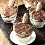 4 tiramisu cups on top of black tray and white saucer.