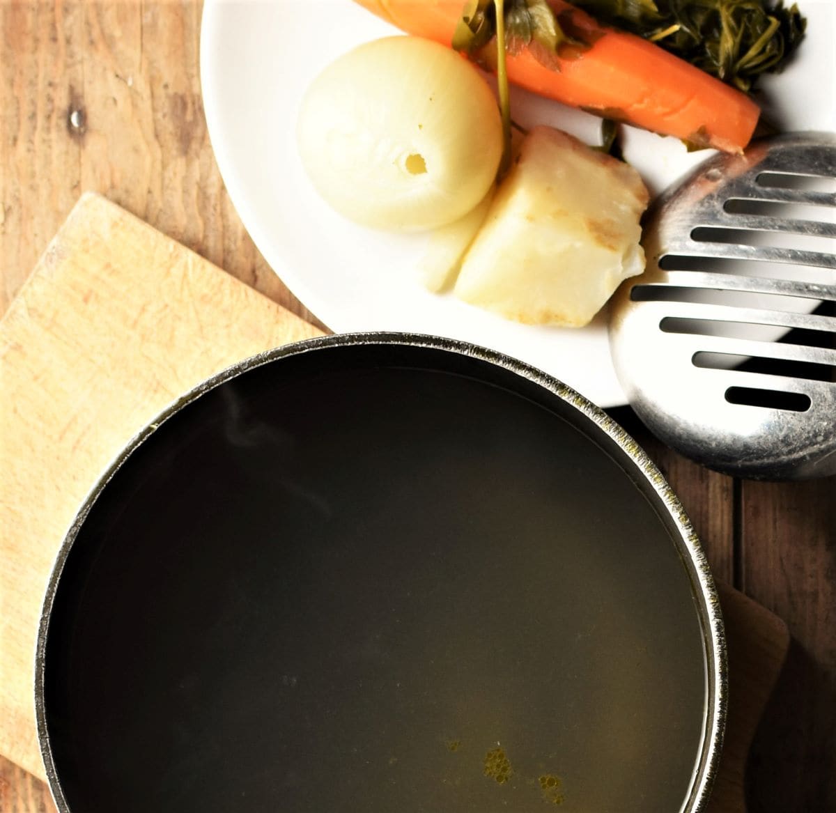 Clear soup in pot and cooked vegetables on plate.