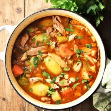 Chicken potato stew with vegetables and herbs in pot.
