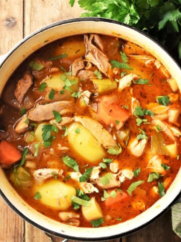 Chicken potato stew with vegetables and herbs in pot.