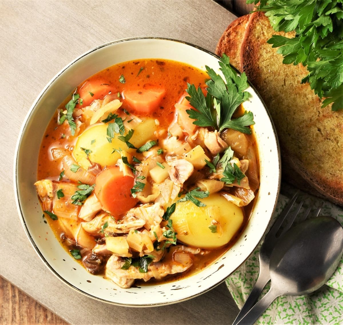 Chicken and potato stew in bowl with vegetables and parsley.
