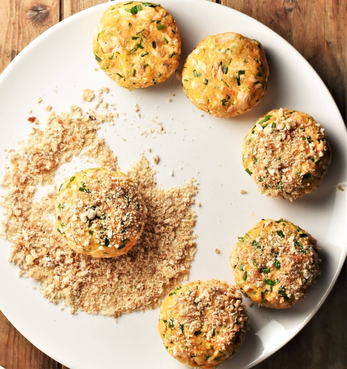 Coating salmon fish cakes in breadcrumbs on large plate.