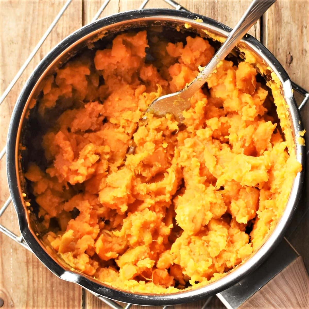 Mashing cooked sweet potato in saucepan with fork.