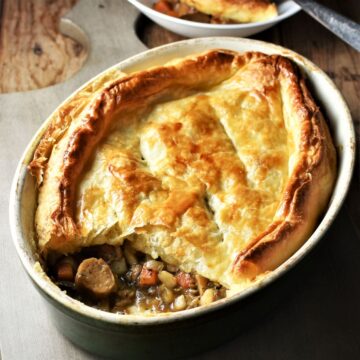 Side view of sausage pie with puff pastry in oval dish.