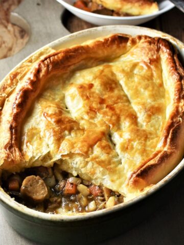 Side view of sausage pie with puff pastry in oval dish.