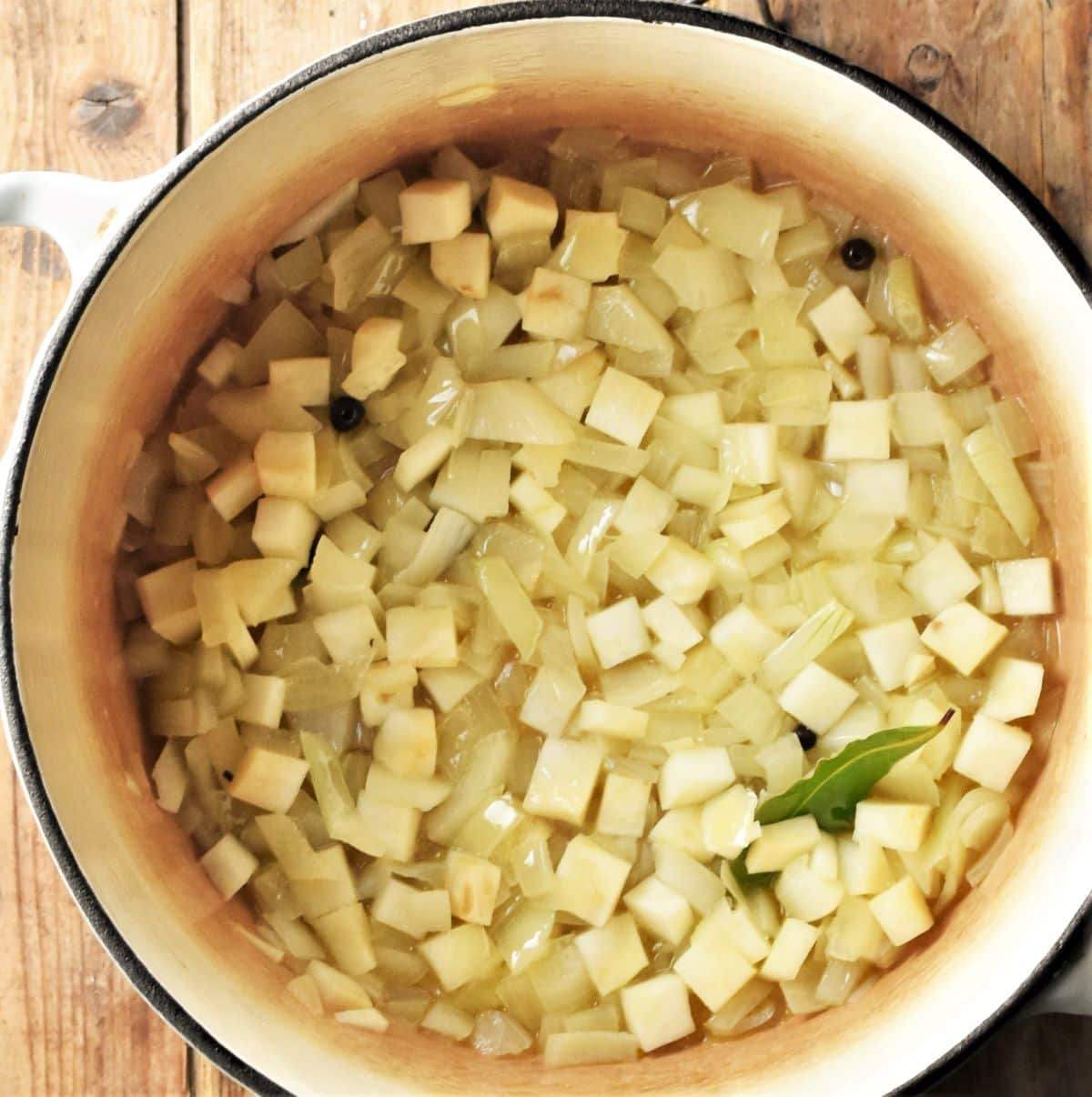 Diced onion and celery root with bay leaf cooking in pot.