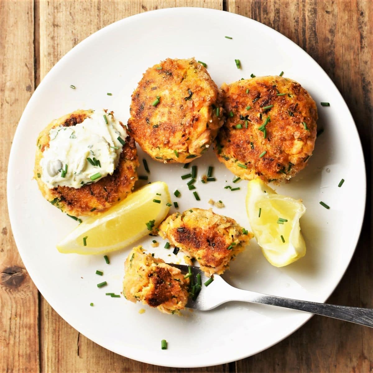 Crispy salmon fish cakes on top of plate with lemon wedges, fork and sauce.