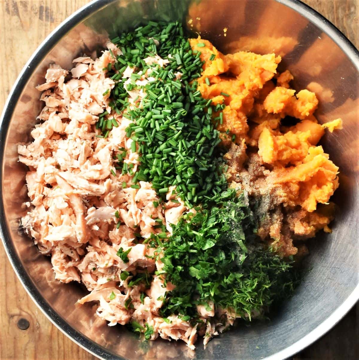 Flaked salmon, mashed sweet potato and chopped herbs in large metal bowl.