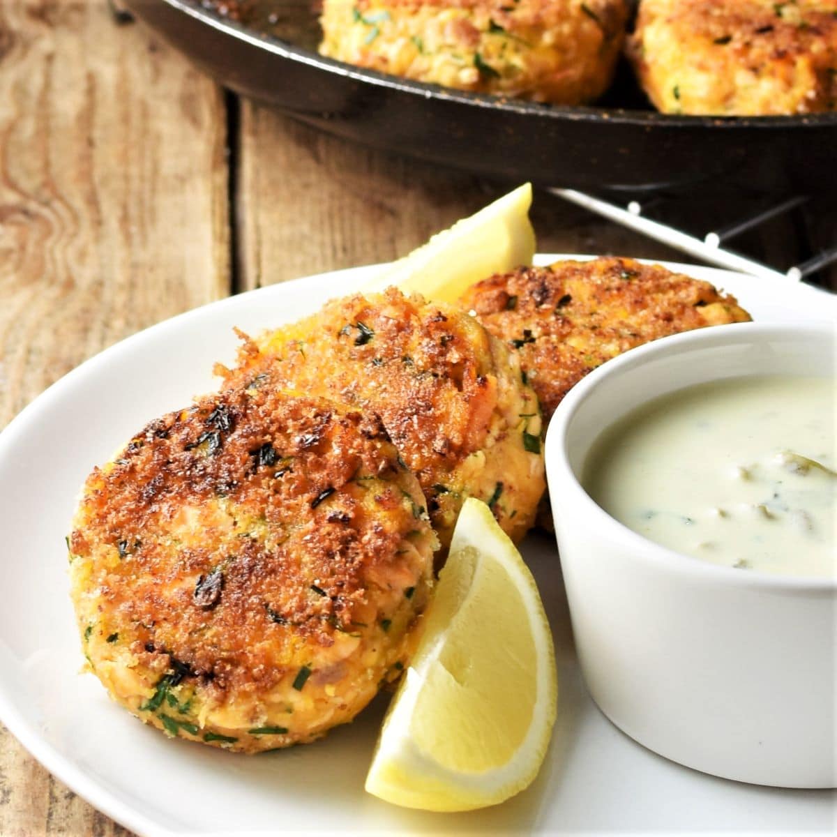 Side view of sweet potato salmon fish cakes on plate with lemon wedge and yogurt dip.