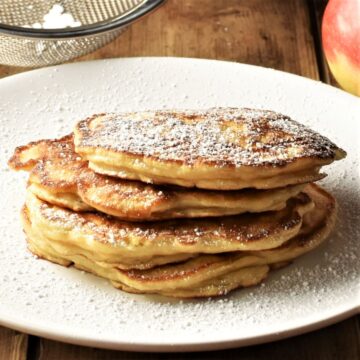 Side view of apple pancakes dusted with icing sugar stacked on plate.