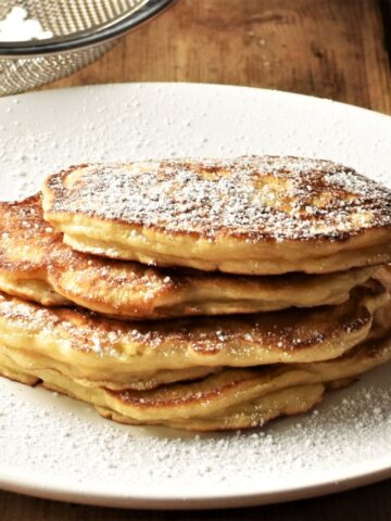 Side view of apple pancakes dusted with icing sugar stacked on plate.